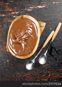 Hazelnut butter in a plate with a spoon. Against a dark background. Top view. High quality photo. Hazelnut butter in a plate with a spoon.
