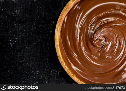 Hazelnut butter in a wooden plate. On a black background. High quality photo. Hazelnut butter in a wooden plate.