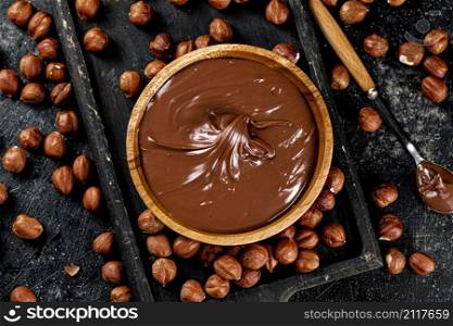 Hazelnut butter on a cutting board with a spoon. On a black background. High quality photo. Hazelnut butter on a cutting board with a spoon.