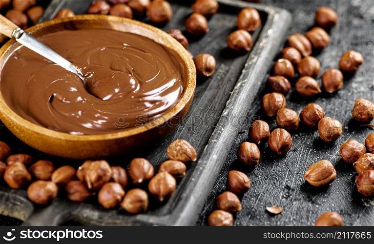 Hazelnut butter on a cutting board with a spoon. On a black background. High quality photo. Hazelnut butter on a cutting board with a spoon.