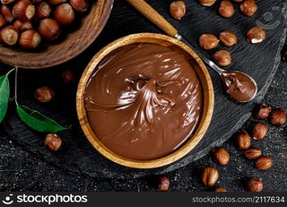 Hazelnut butter on a stone board on a plate and in a spoon. On a black background. High quality photo. Hazelnut butter on a stone board on a plate and in a spoon.