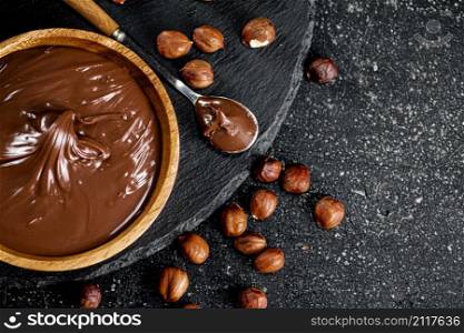 Hazelnut butter on a stone board on a plate and in a spoon. On a black background. High quality photo. Hazelnut butter on a stone board on a plate and in a spoon.