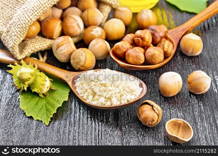 Hazelnut flour in a spoon, nuts in a bag, spoon and on the table, oil in glass jar and filbert branch with green leaves on wooden board background