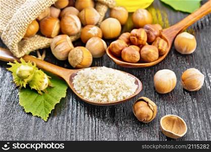 Hazelnut flour in a spoon, nuts in a bag, spoon and on the table, oil in glass jar and filbert branch with green leaves on wooden board background