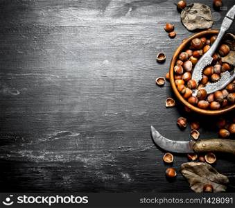 Hazelnuts in a bowl with a Nutcracker and an old knife. On the black wooden table.. Hazelnuts in a bowl