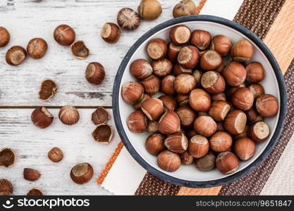 Hazelnuts in enamel bowl and napkin on white wooden table, top view