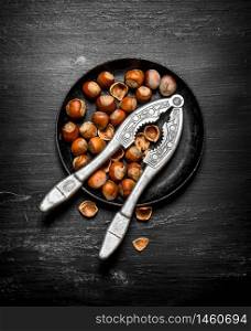 Hazelnuts with Nutcracker on the old plate. On the black wooden table.. Hazelnuts with Nutcracker on the old plate.