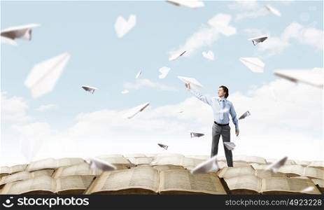 He doesn&rsquo;t take life too seriously. Young businessman in pile of books with paper plane in hand