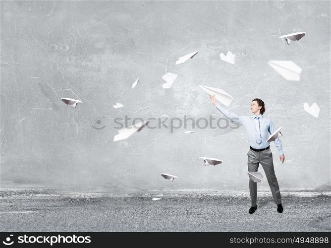 He doesn&rsquo;t take life too seriously. Young businessman in concrete room with paper plane in hand