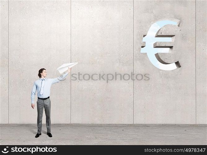 He doesn&rsquo;t take life too seriously. Young businessman in concrete room with paper plane in hand