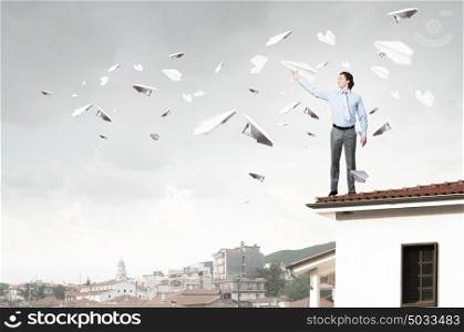 He doesn&rsquo;t take life too seriously. Young businessman in pile of books with paper plane in hand
