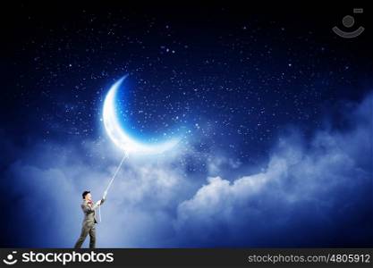 He gets what he wants. Young businessman in hat who obtains moon with rope