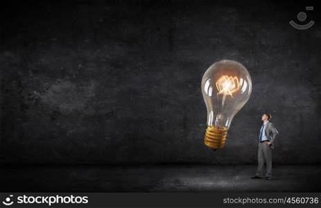 He has big bright idea. Young businessman in darkness looking at glowing light bulb