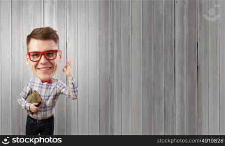 He has great mind. Young funny big headed man in glasses with book in hands showing ok gesture