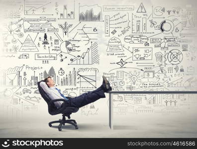 He is bosy and relaxed. Smiling businessman sitting in chair with legs on table