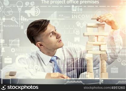 He is building his business. Young businessman making pyramid with empty wooden cubes