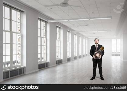 He is carrying out an idea. Elegant businessman in modern office with huge bulb in hands