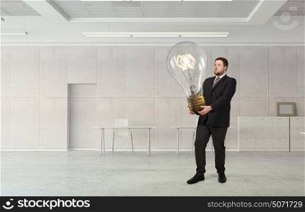 He is carrying out an idea. Elegant businessman in modern office with huge bulb in hands
