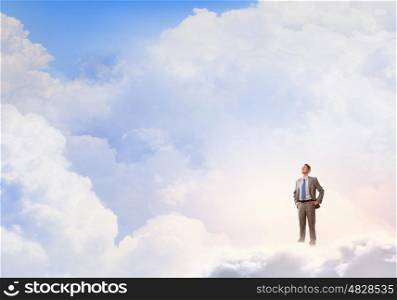 He is confident in his success. Young confident businessman with arms on waist standing on cloud
