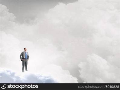 He is confident in his success. Young confident businessman with arms on waist standing on cloud