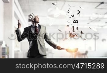 He is cooking something special. Young man in business suit and cook hat holding pan