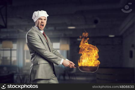 He is cooking something special. Young man in business suit and cook hat holding pan