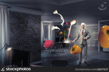 He is cooking something special. Young man in business suit and cook hat holding pan