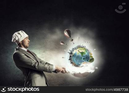 He is cooking something special. Young man in business suit and cook hat holding pan. Elements of this image are furnished by NASA