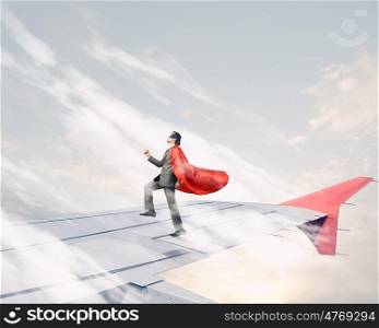 He is flying high. Super man standing on edge of airplane wing