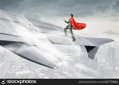 He is flying high. Super man standing on edge of airplane wing