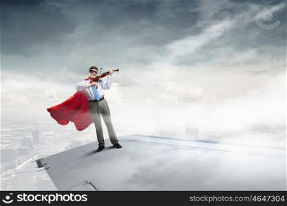 He is flying high. Super man standing on edge of airplane wing playing violin