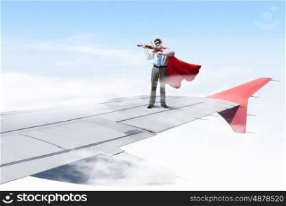 He is flying high. Super man standing on edge of airplane wing playing violin