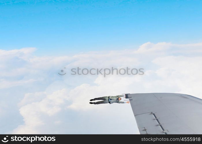 He is flying high. Young businessman hanging on edge of airplane wing