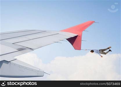 He is flying high. Young businessman hanging on edge of airplane wing