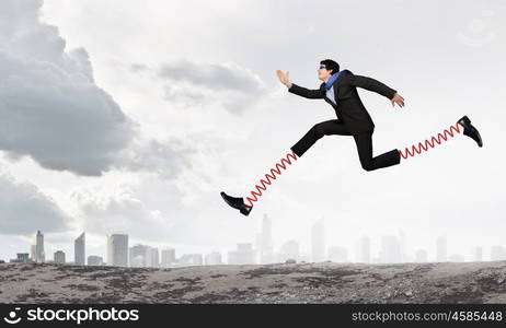 He is making giant steps. Businessman in suit running with big springs on feet