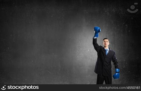 He is ready to fight for success. Young businessman in blue boxing gloves on dark background