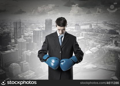 He is ready to fight for success. Young businessman in blue boxing gloves on city background