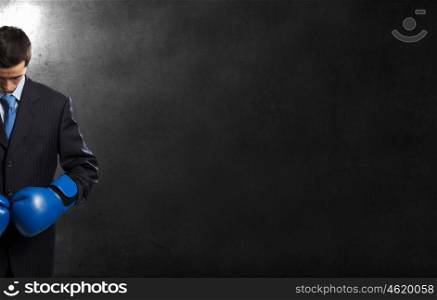 He is ready to fight for success. Young businessman in blue boxing gloves on dark background