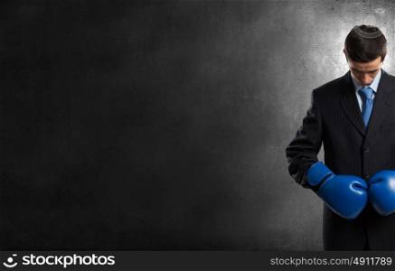 He is ready to fight for success. Young businessman in blue boxing gloves on dark background