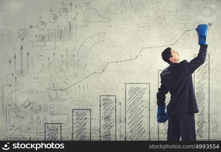 He is ready to fight for success. Young businessman in boxing gloves on cement background