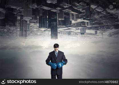 He is ready to fight for success. Young businessman in boxing gloves on city background