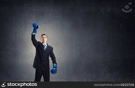 He is ready to fight for success. Young businessman in boxing gloves on dark background