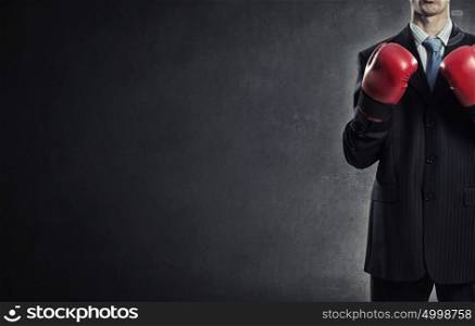 He is ready to fight for success. Young businessman in boxing gloves on dark background