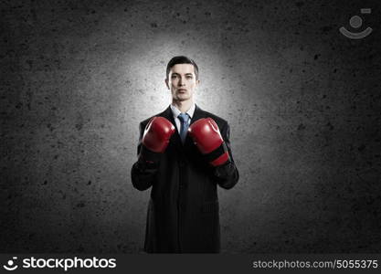 He is ready to fight for success. Young businessman in red boxing gloves on dark background