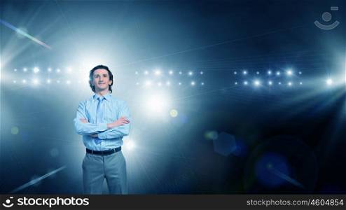 He is ready to performe. Businessman with arms crossed on chest standing in lights of stage
