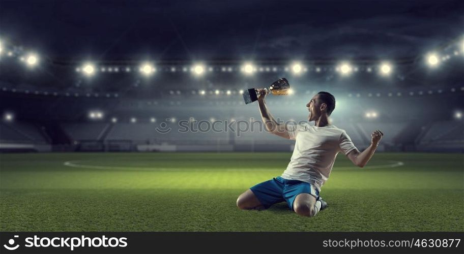 He is the champion. Soccer player celebrating victory while holding win cup