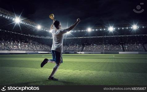 He is the champion. Soccer player celebrating victory while holding win cup