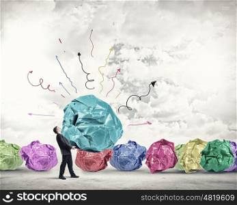 He is working hard on his new idea. Businessman carrying with effort big crumpled ball of paper as creativity sign