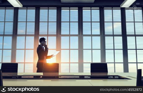 He is working till sundown. Mixed media. Elegant businessman in office in light of sunset