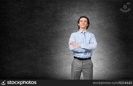 He is young professional. Young confident businessman with arms crossed on chest against concrete background